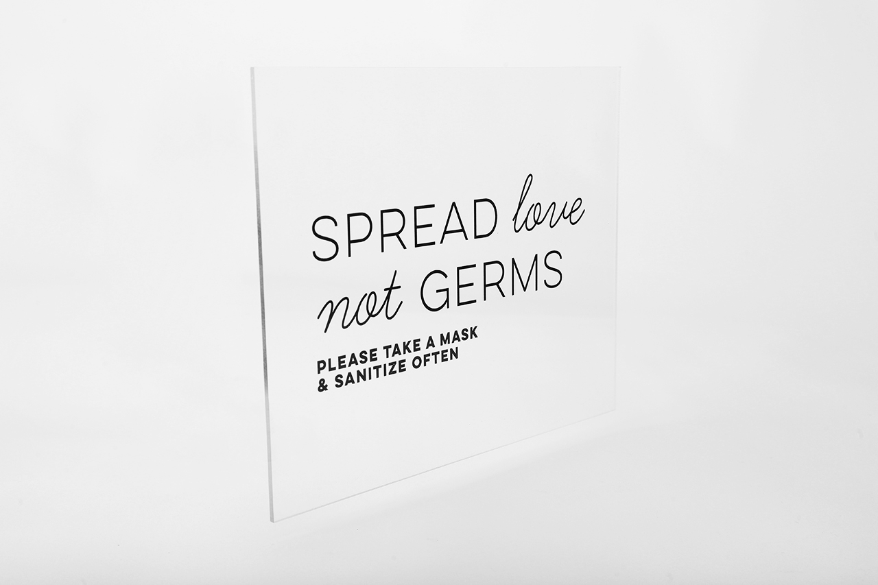 An acrylic sign that says Spread Love Not Germs in black letters.