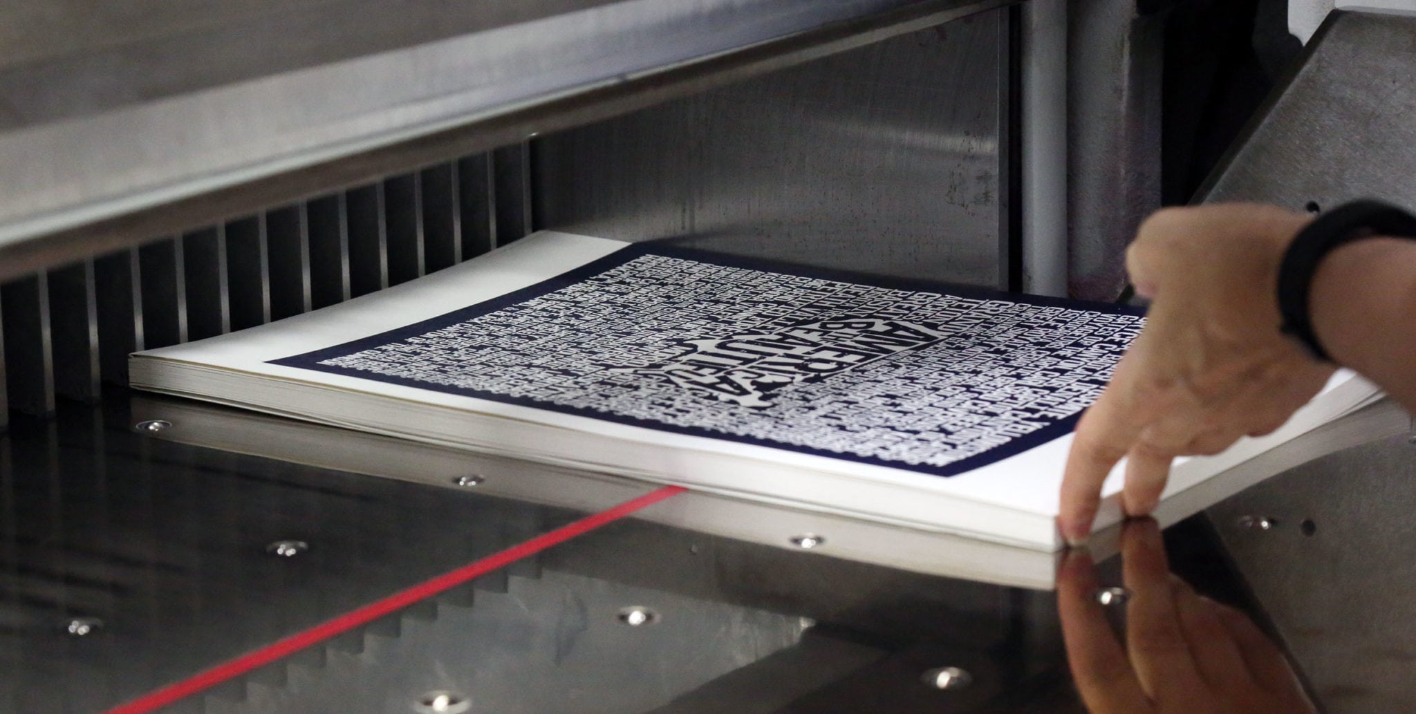 A hand aligning a stack of custom posters in a printer.