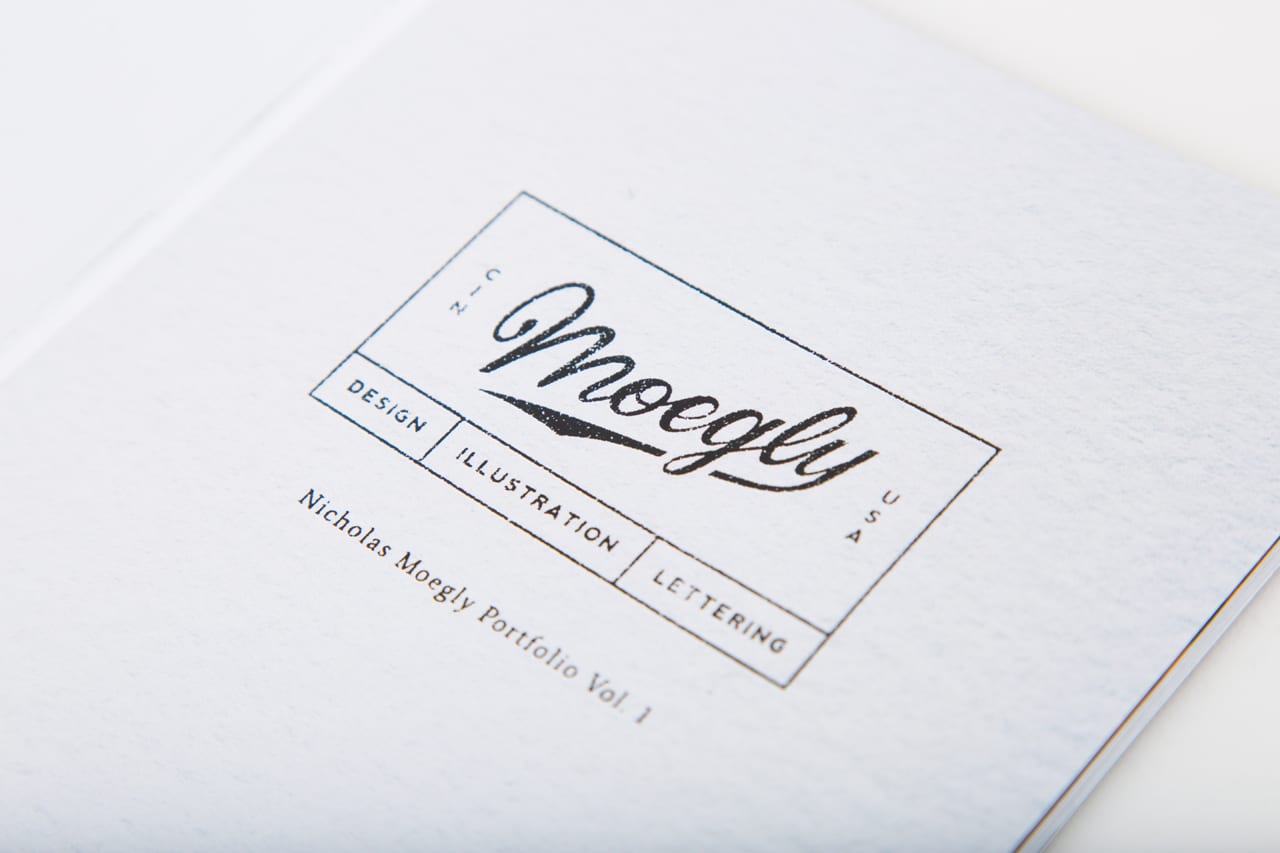 A photography portfolio with a white cover and printed with Moegly in black swirling letters.