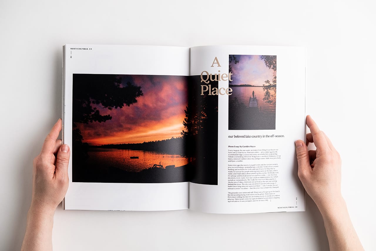 Two hands holding open a magazine printed with images of a sunset over a lake and A Quiet Place.