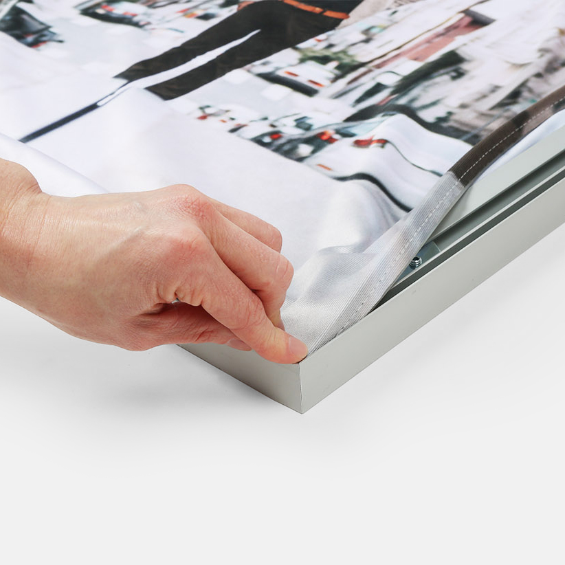 A hand stretching an SEG fabric graphic into the corner of its aluminum frame.