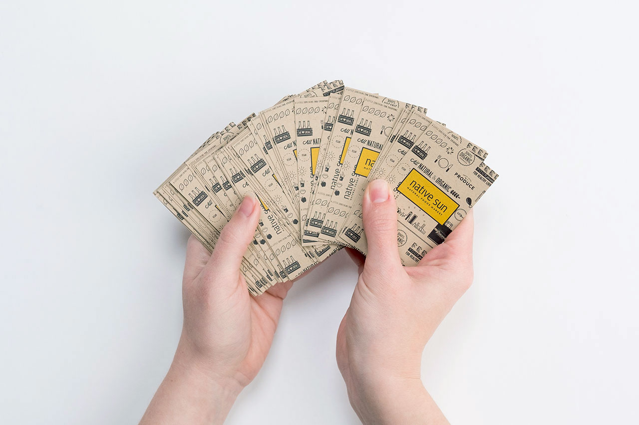 Two hands holding fanned-out business cards printed with Native Sun on Kraft paper.