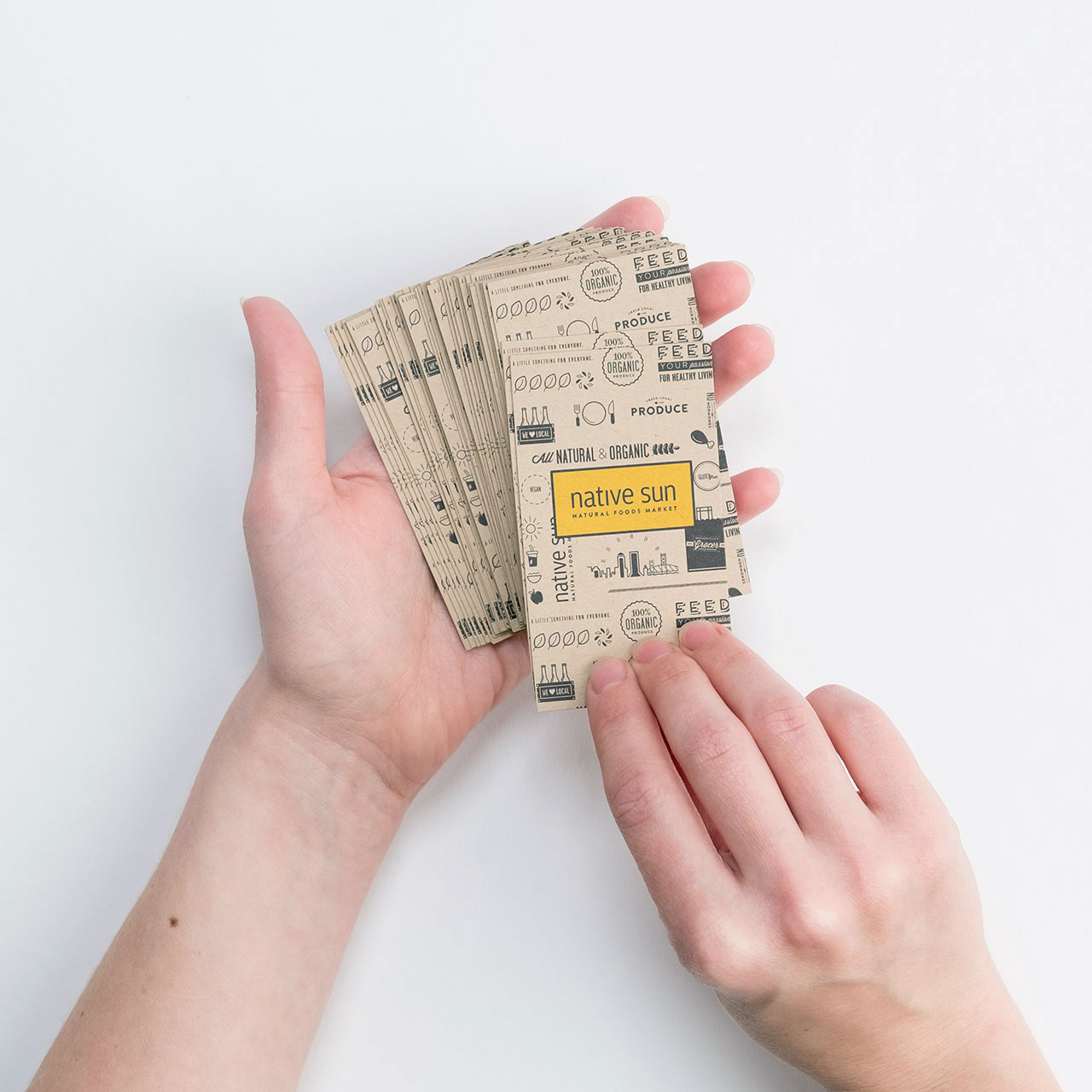 Two hands holding a stack of fanned-out business cards printed on Kraft paper.