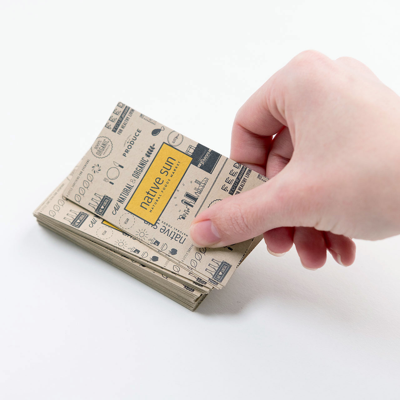 A stack of custom business cards printed on Kraft paper with a hand taking the one off the top.