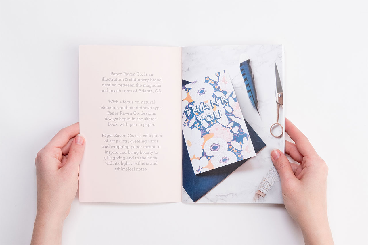 Two hands holding open a product catalog to an image of custom stationery and brand information.