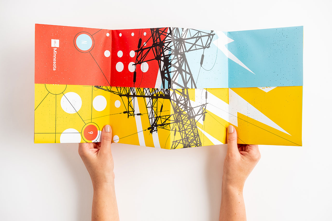 Two hands holding open a creative mailer designed in bright orange, yellow, white and teal.