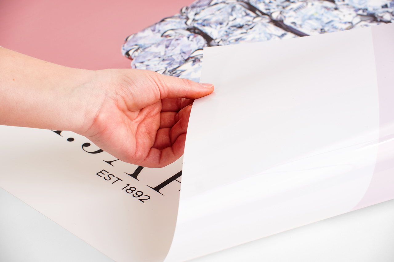 A hand rolling back the corner of a jewelry marketing poster printed with a pink design.