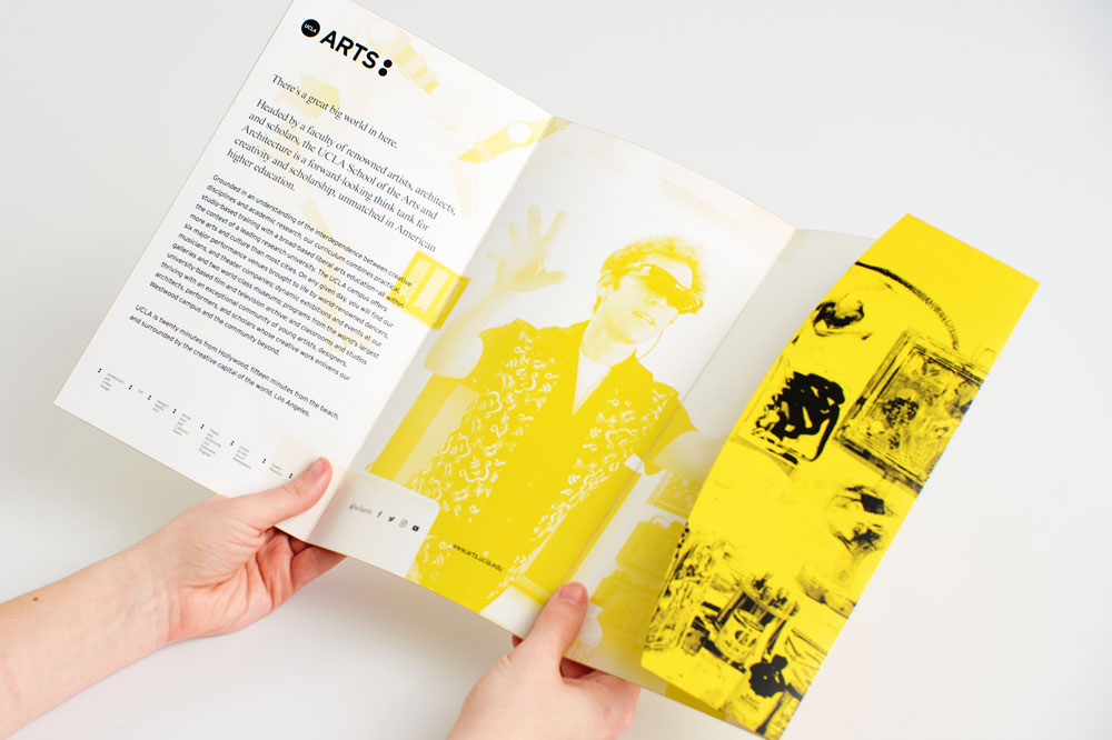 Two hands holding open an unfolded tri-fold pocket mailer with a black, yellow and white design.