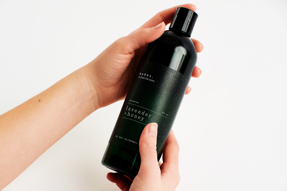 Two hands holding a shampoo bottle with a custom label printed with a silver and green design.