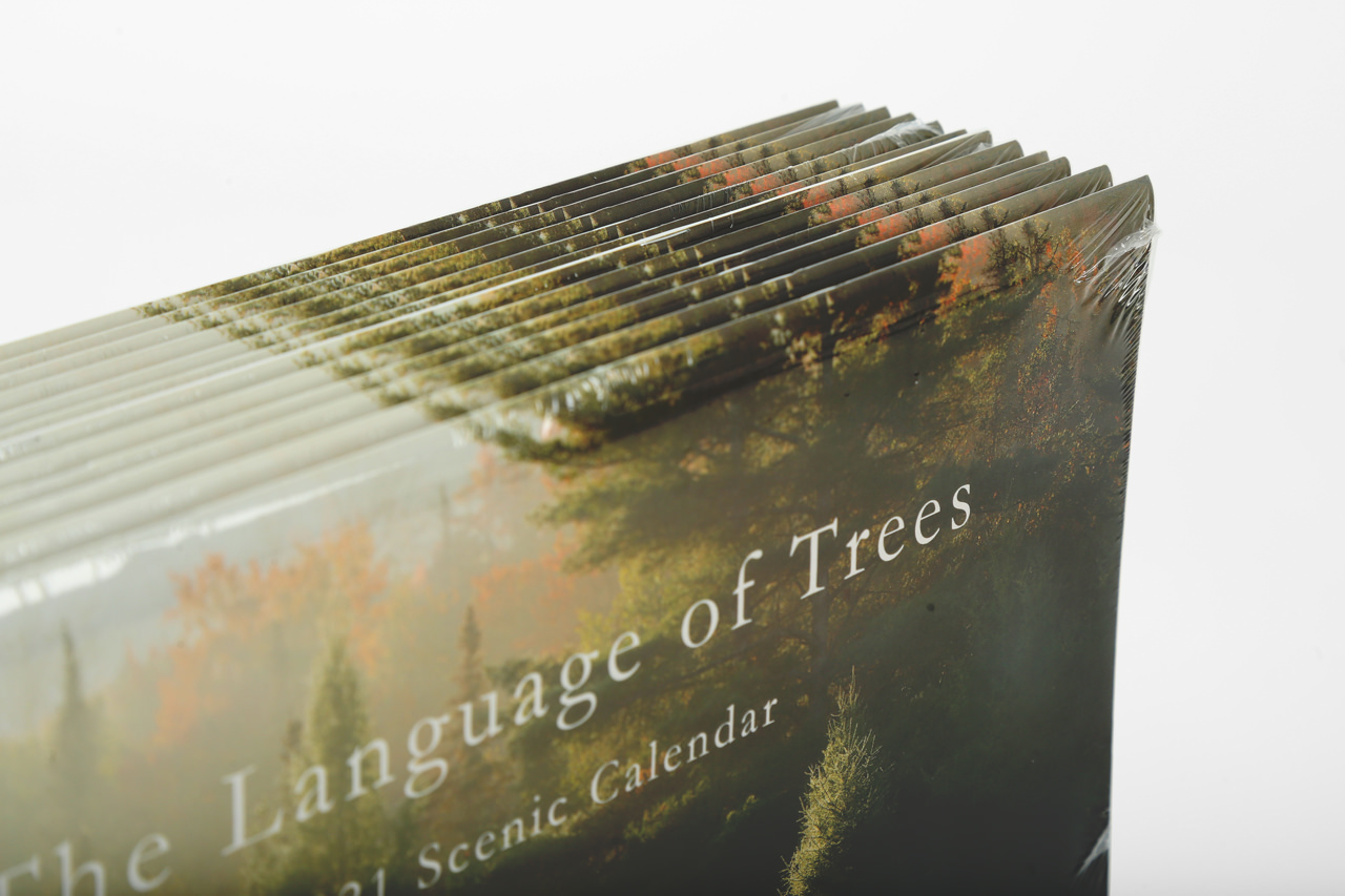 A stack of wall calendars with The Language of Trees on the cover and shrink wrapped for retail.