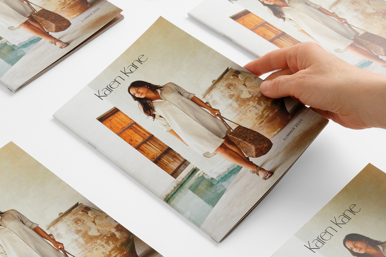 A hand picking up a saddle stitch booklet with a woman in a dress on the cover.