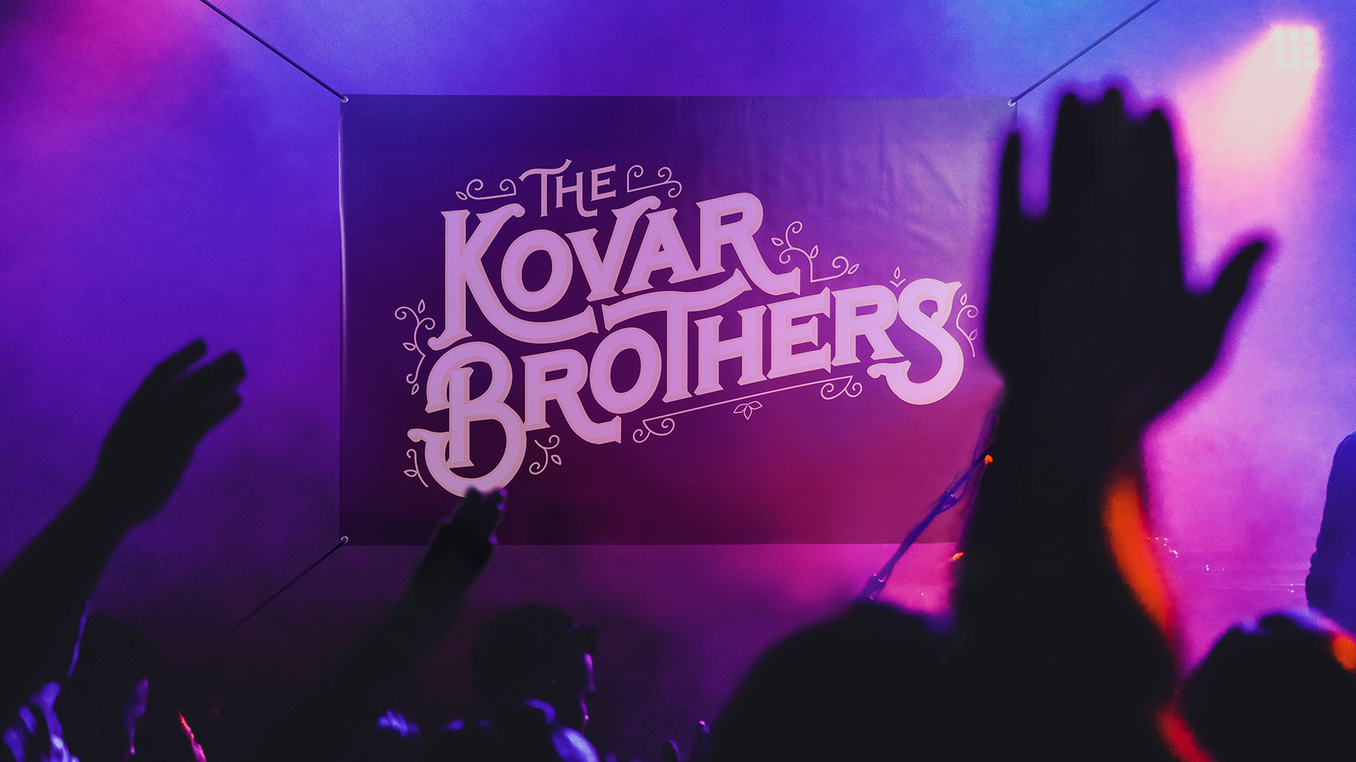 A custom banner printed with The Kovar Brothers hanging over a stage in front of a crowd.