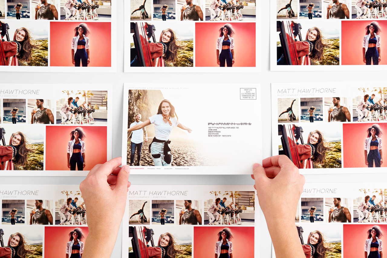 Two hands holding a direct mail postcard with more postcards all around it.