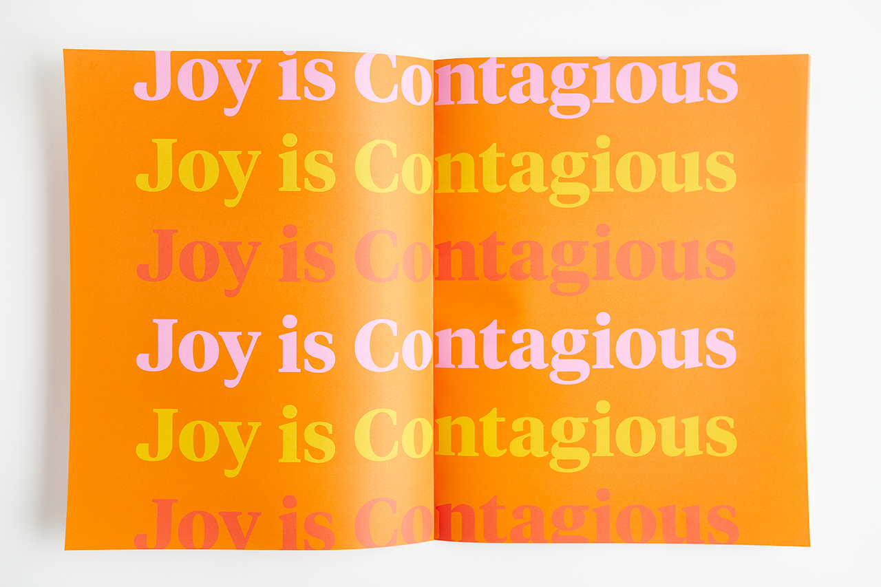 A booklet laying open and printed with Joy is Contagious in orange, pink, yellow and red.