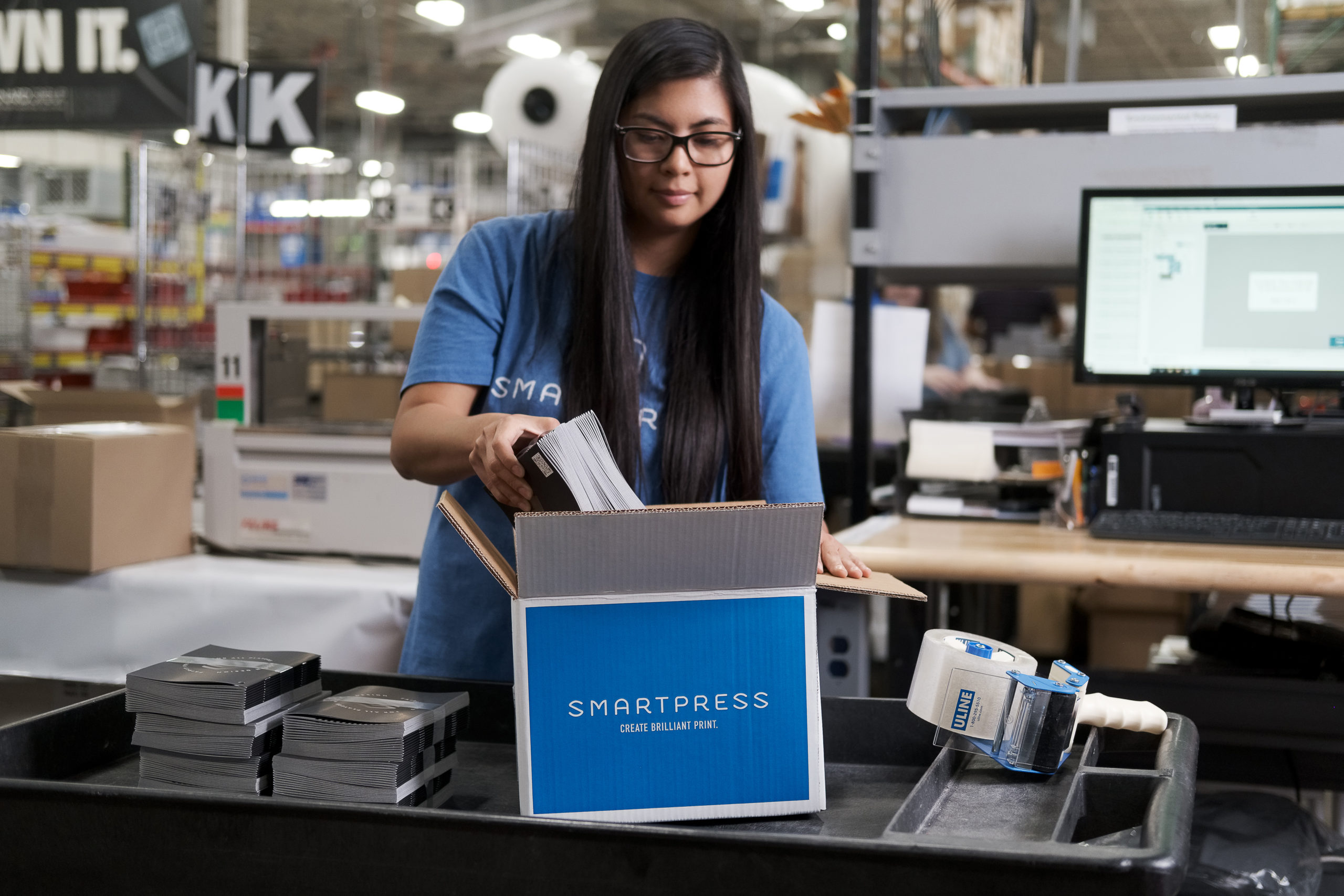 A woman with long black hair putting bundles of print assets into a Smartpress box.