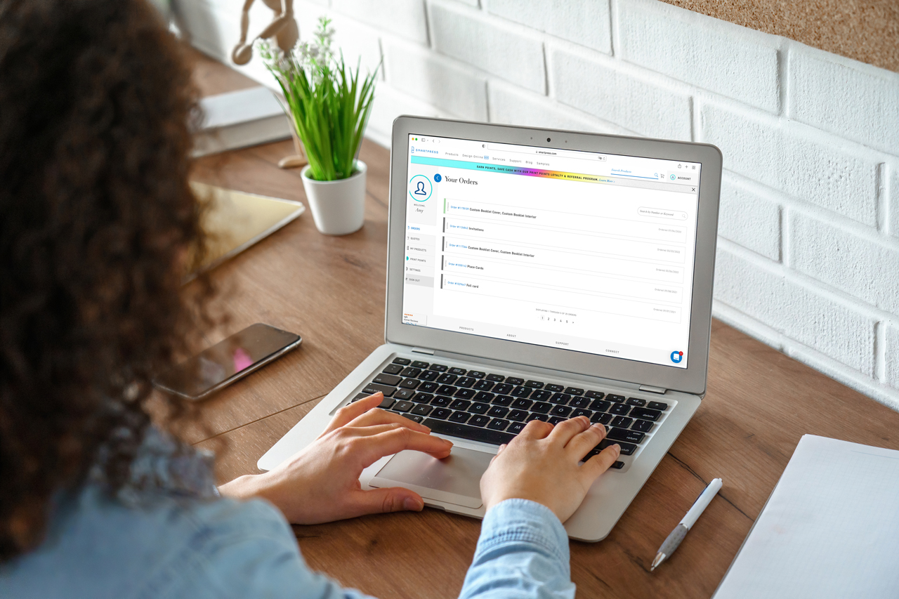 A woman typing on a laptop that's sitting on a wooden desk with other stationery.