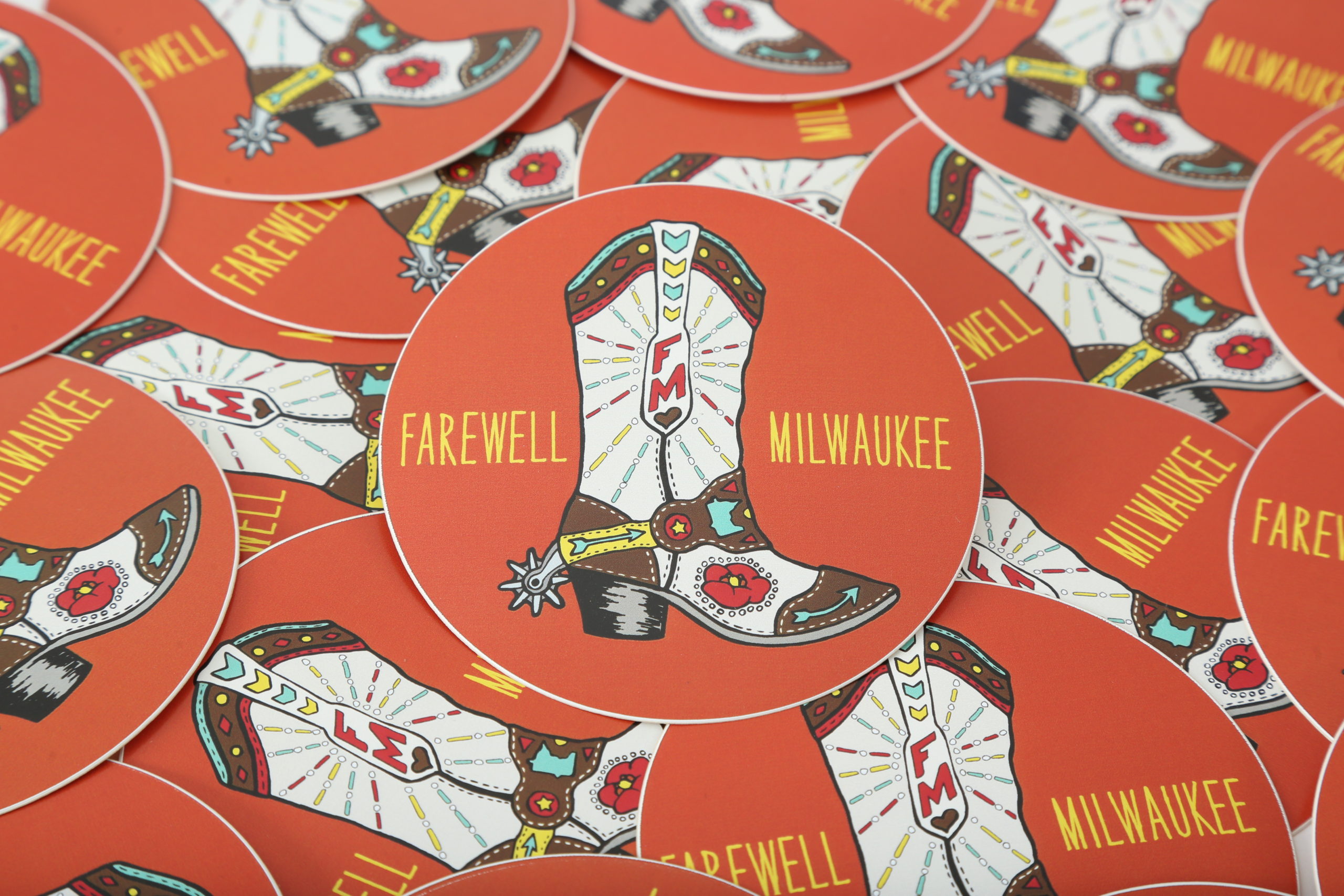 A pile of scattered stickers with an orange background, cowboy boot and Farewell Milwaukee in yellow.
