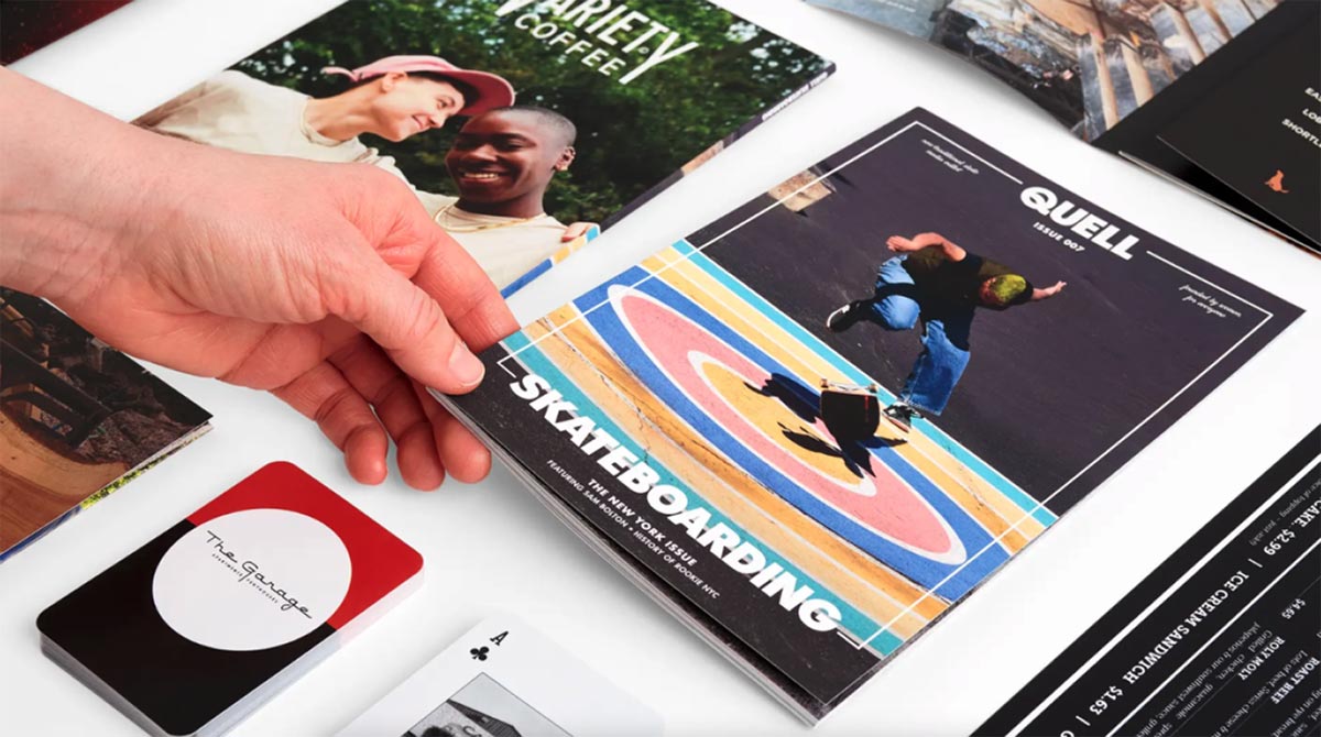 A hand laying a booklet on a table with other booklets and playing cards around it.